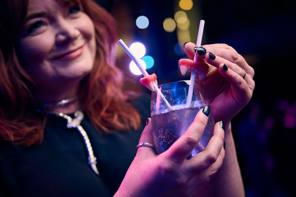 A woman wearing a witch costume holding a cocktail with candy teeth impaled on straws.