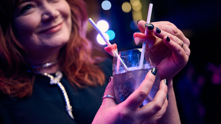 A woman wearing a witch costume holding a cocktail with candy teeth impaled on straws.