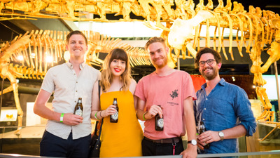 Four friends enjoying a beer in front of dinosaur skeletons in Dinosaur Walk.