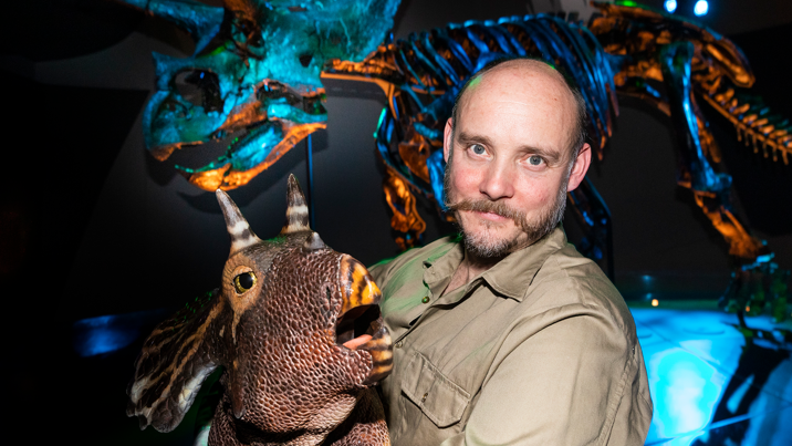 A man poses with a baby triceratops in front of Horridus, the triceratops fossil found at Melbourne Museum.