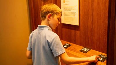  Primary school student interacting with display in Getting In exhibition in Immigration Museum.