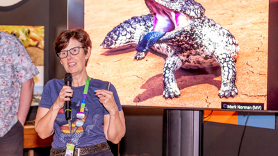 A woman in front of a screen displaying a blue-tongued lizard gives a talk.