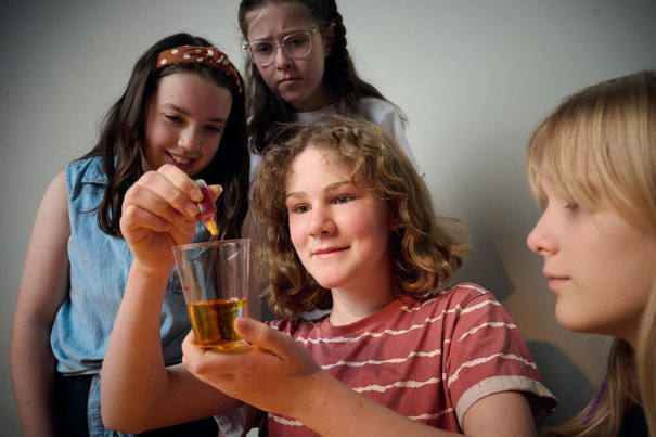 Three young adults look on as another adds drops of reagent to a glass of liquid as part of a science experiment during Science Studio workshop at Scienceworks.