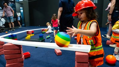 Child wearing a hardhat rolls a ball down a ramp as part of the Roll Zone at Scienceworks.