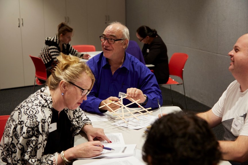 Three Smiling Teachers Work Together On Wooden Stick Structure