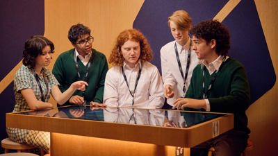 A group of students in the Road to Zero Learning Studio standing and sitting around a touch table 