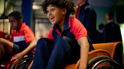 A primary school student excitedly participates in the wheelchair race in Sportsworks while on an excursion. 
