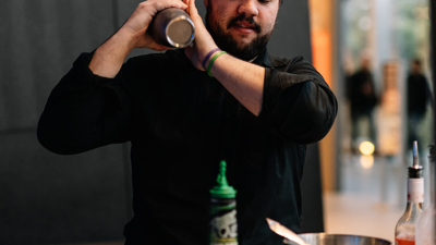 A bar-person prepares a cocktail in a shaker.