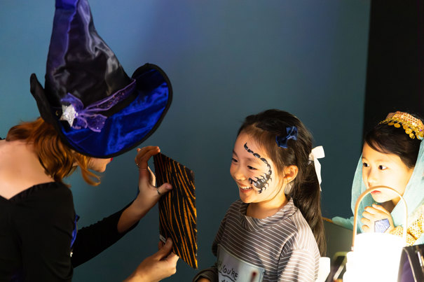 A little girl smiles with enjoyment as she is shown the painted scorpion on her face during Halloween at the Museum.