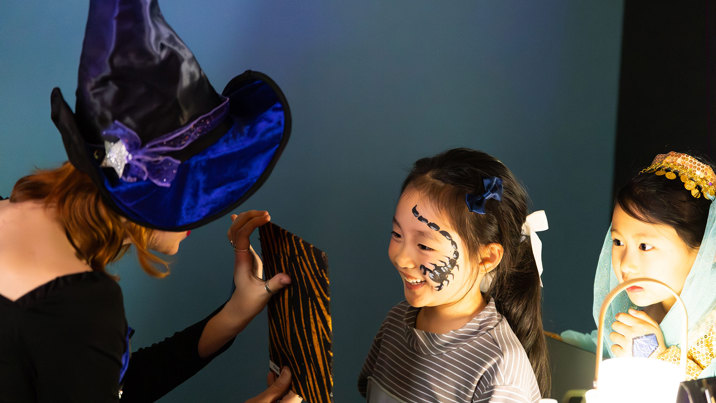 A little girl smiles with enjoyment as she is shown the painted scorpion on her face during Halloween at the Museum.