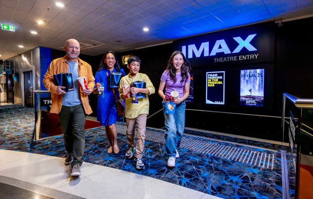 Family in the IMAX foyer carrying popcorn and drinks during a Family sleepover at Melbourne Museum.