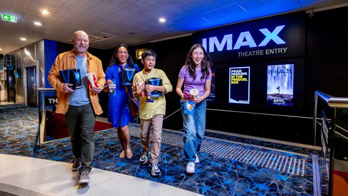 Family in the IMAX foyer carrying popcorn and drinks during a Family sleepover at Melbourne Museum.
