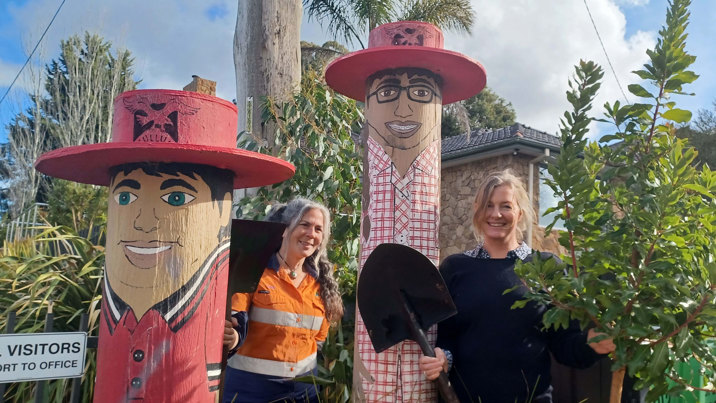 Two women with shovels stand near trees