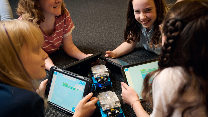 Young adults gather in a circle, working together to program their robots on iPads as part of Robots and Coding workshop at Scienceworks.