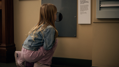 A girl uses a porthole display in Leaving Home exhibition at the Immigration Museum.