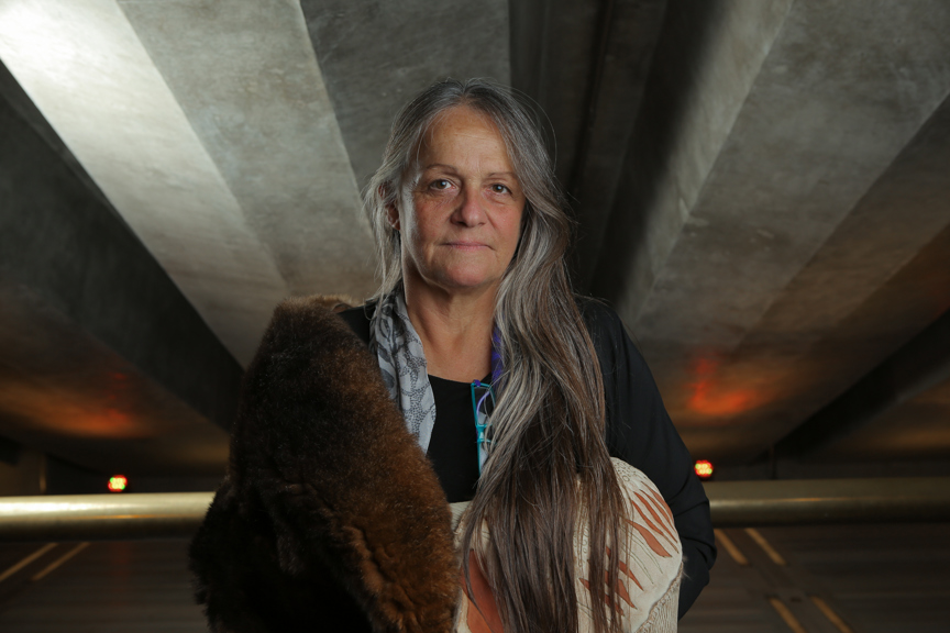 Portrait of a woman in a carpark wrapped in a possum skin cloak. 