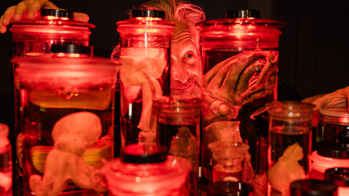 A museum expert crouches behind a wall of marine animal collections preserved in jars during Halloween at the Museum.