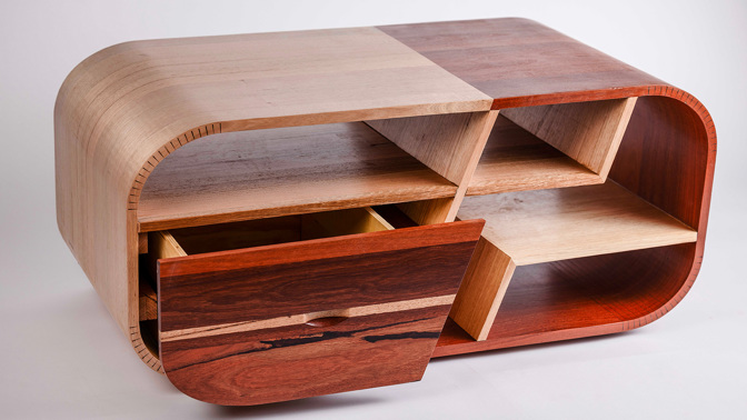 A rounded wooden coffee table with a drawer and shelves
