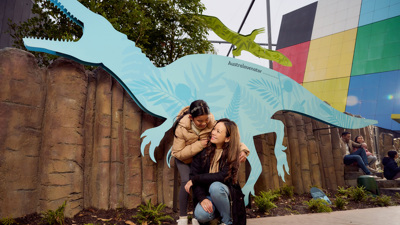 A girl and woman pose in front of the Australovenator in metal cut out in the Gandel Gondwana Garden