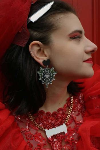 Woman with a knife in her hair wearing spider web earrings and a zombie fang necklace.