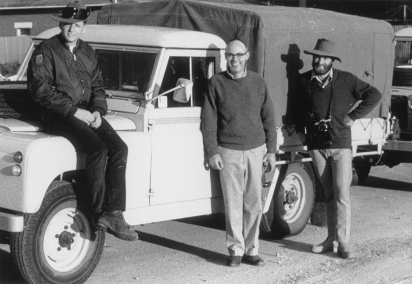 A black and white photo of three people next to a car