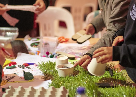 A table with craft materials and hands are visible putting things together.