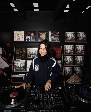 Steely Ann standing infront of a record dj deck with vynls in the background.