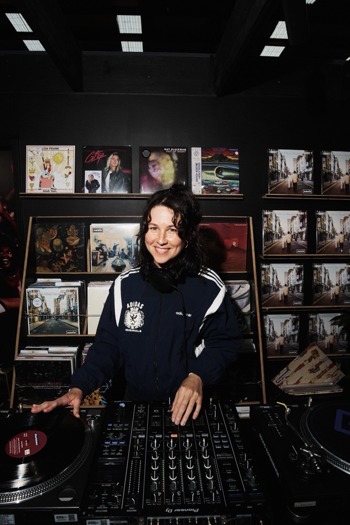 Steely Ann standing infront of a record dj deck with vynls in the background.