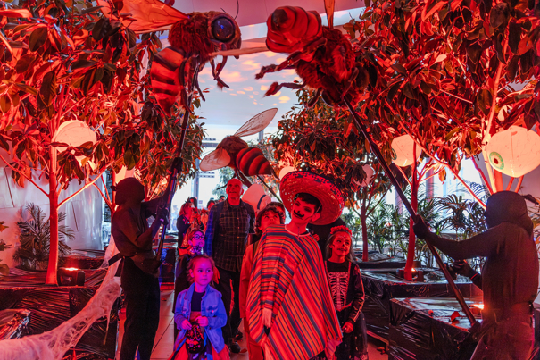 Families entering Halloween at the Museum via a boulevard of trees and puppeteers animating giant bees above their heads.