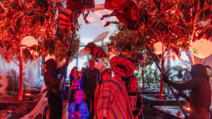 Families entering Halloween at the Museum via a boulevard of trees and puppeteers animating giant bees above their heads.