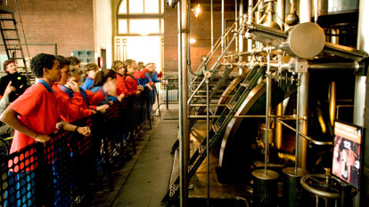 School children watch look at a steam engine that powers a pump 