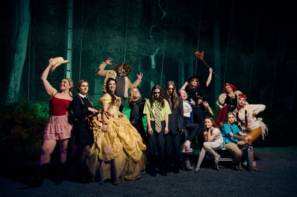 A group of people dressed up in assorted Halloween costumes pose in front of the formidable forest.